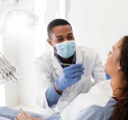 A hygienist and a patient in a bright operatory. The African American hygienist has paused his efforts while his patient answers a question. Behind his mask, you can tell the hygienist is smiling at his patient's response.